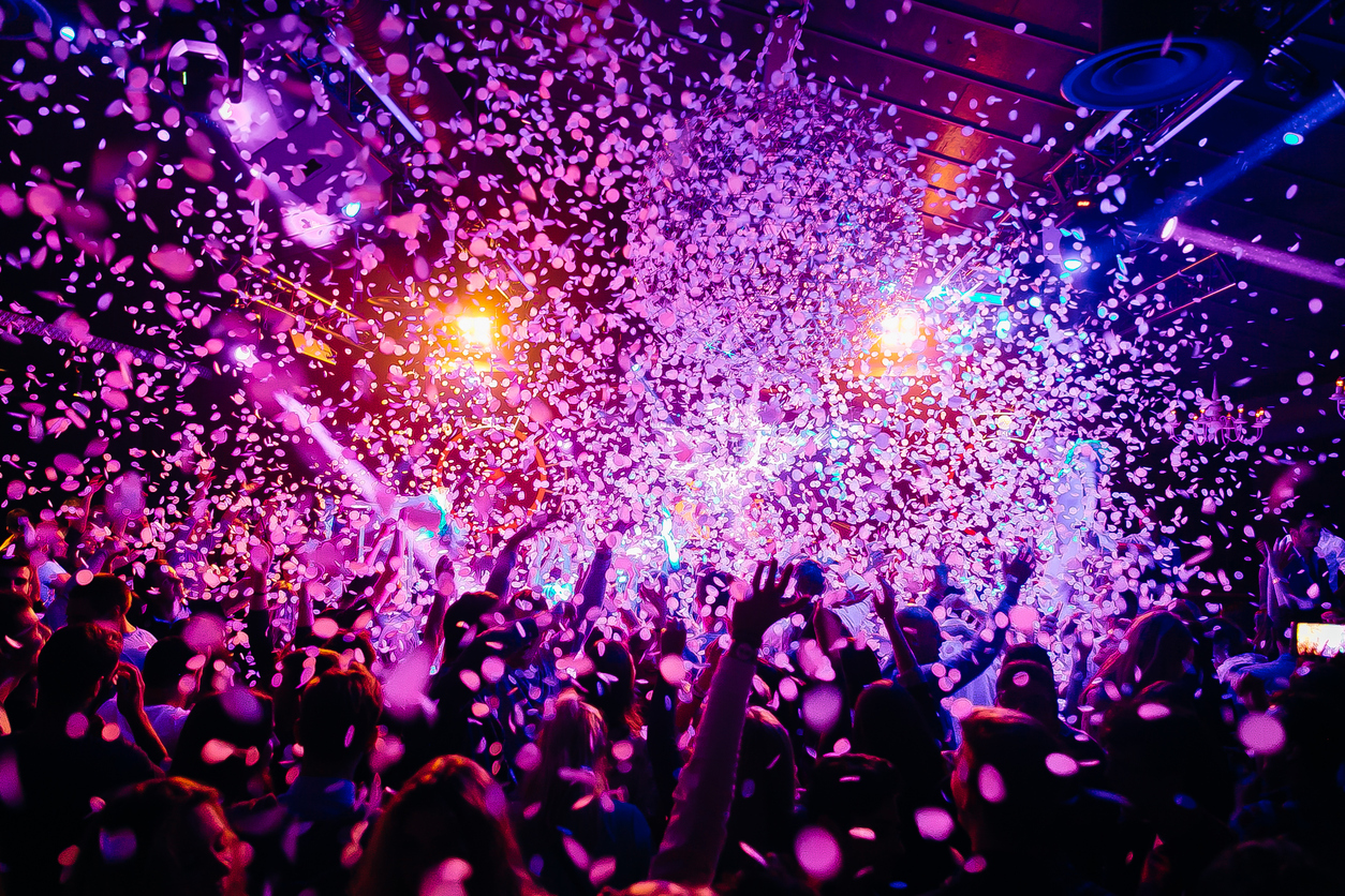 A crowd of people inside a dark nightclub celebrating as confetti falls from the ceiling all around them, representing MI online poker players who may soon be virtually partying with players in other states via a new gaming compact.