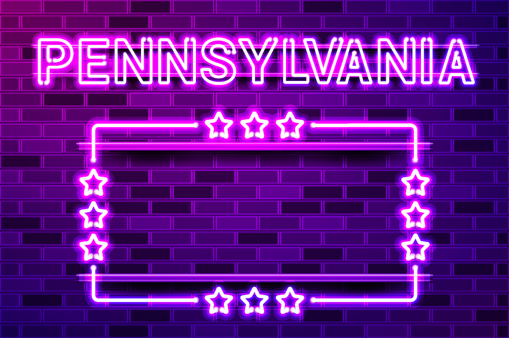 a glowing neon sign on a brick wall that says Pennsylvania with stars in a rectangle below it. A comprehensive guide to the Pennsylvania's online poker rooms: welcome bonuses, promos, MTTs, mobile apps, & everything you need to know to play in PA.